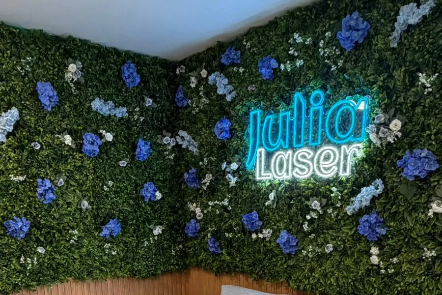 Logo Julia Laser em neon na parede de folhagem da recepção